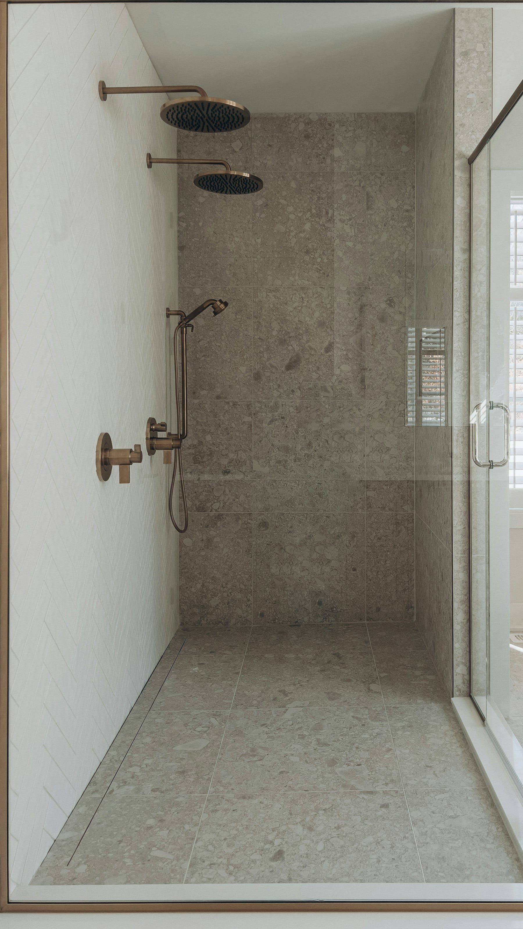 Walk-in shower with speckled terrazzo-style tile, a glass door and brushed-brass rain and hand showers