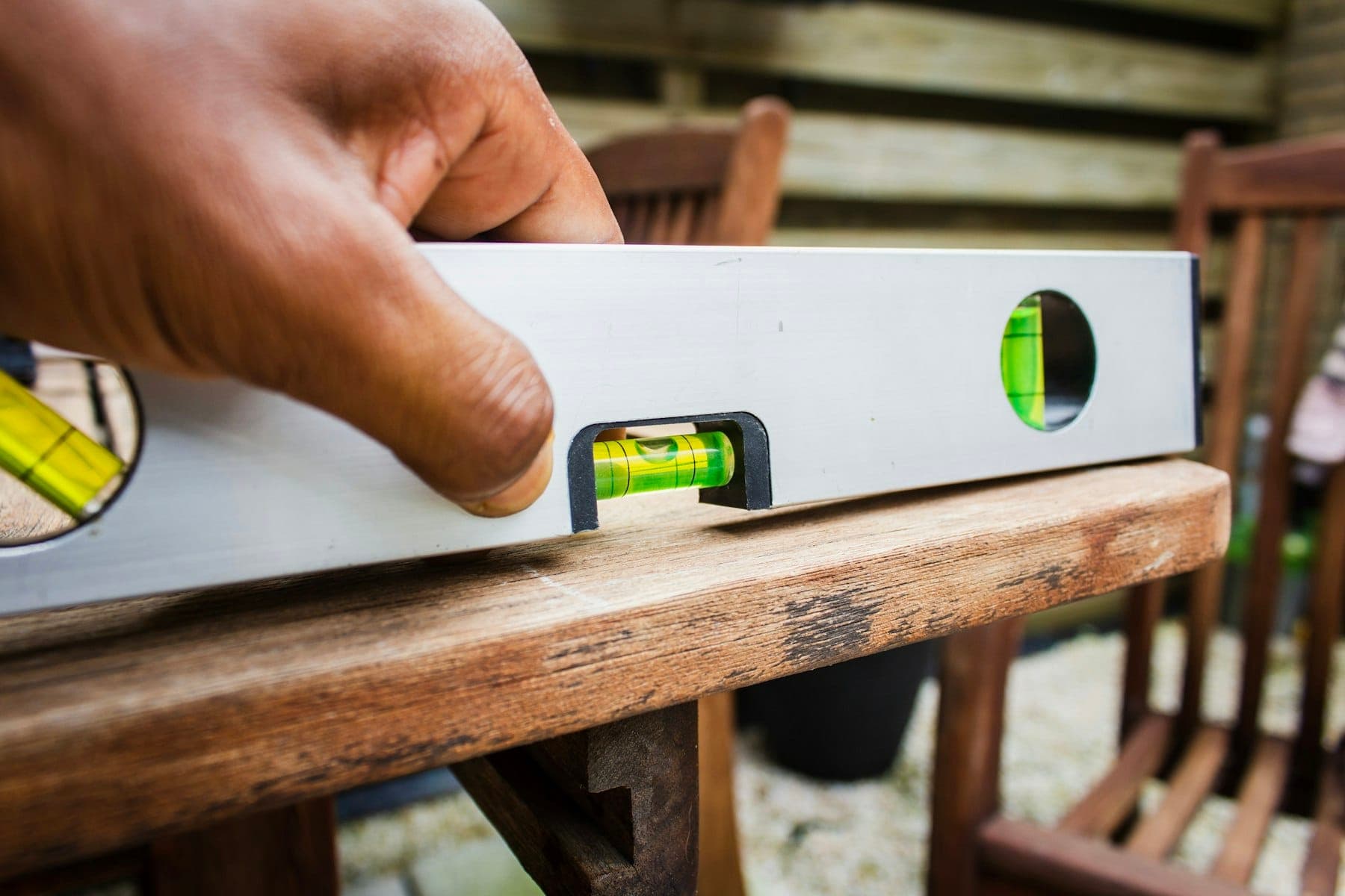 Hand steadying an aluminum spirit level with a centred green bubble on a wooden surface
