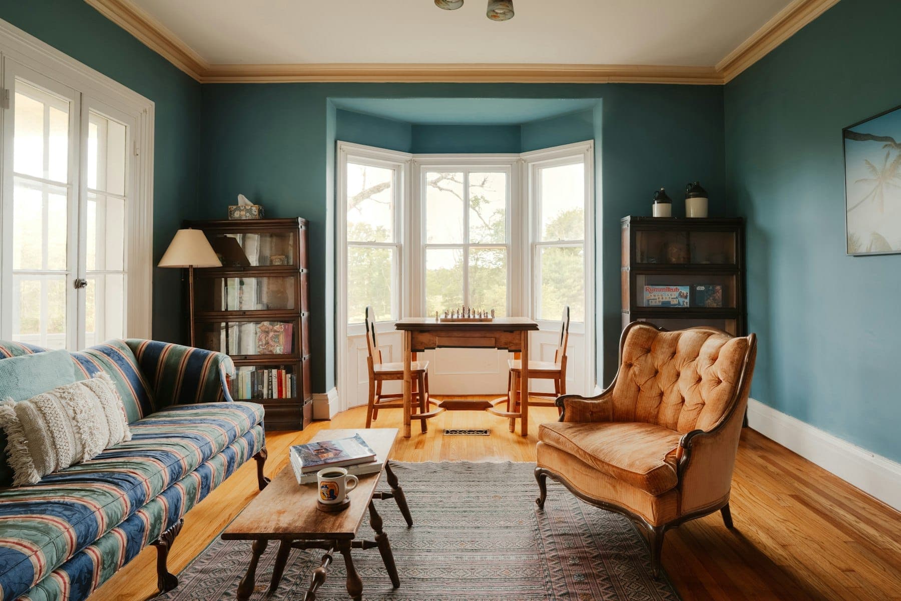 Living room with teal walls, white window and baseboard trim, a bay window and warm wood floors