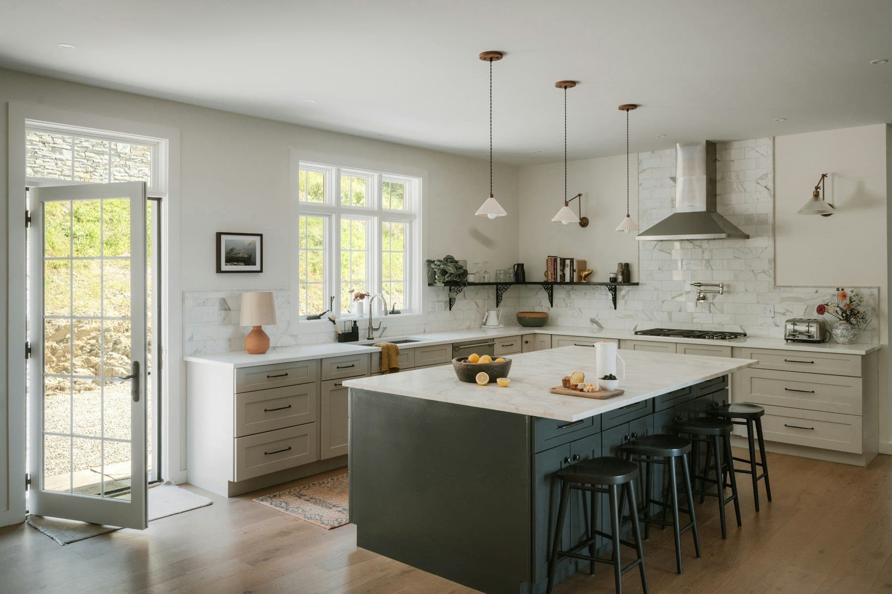 Bright kitchen with light shaker cabinets, a dark island with marble-look top, pendant lights and a glazed garden door