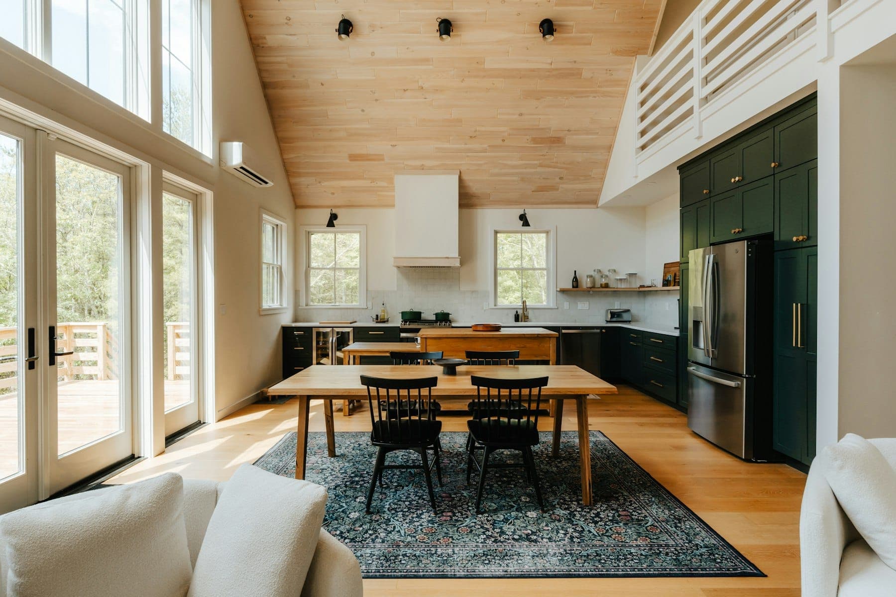 Finished open-plan living and dining space with a vaulted pine ceiling, dark green cabinetry and tall glass doors
