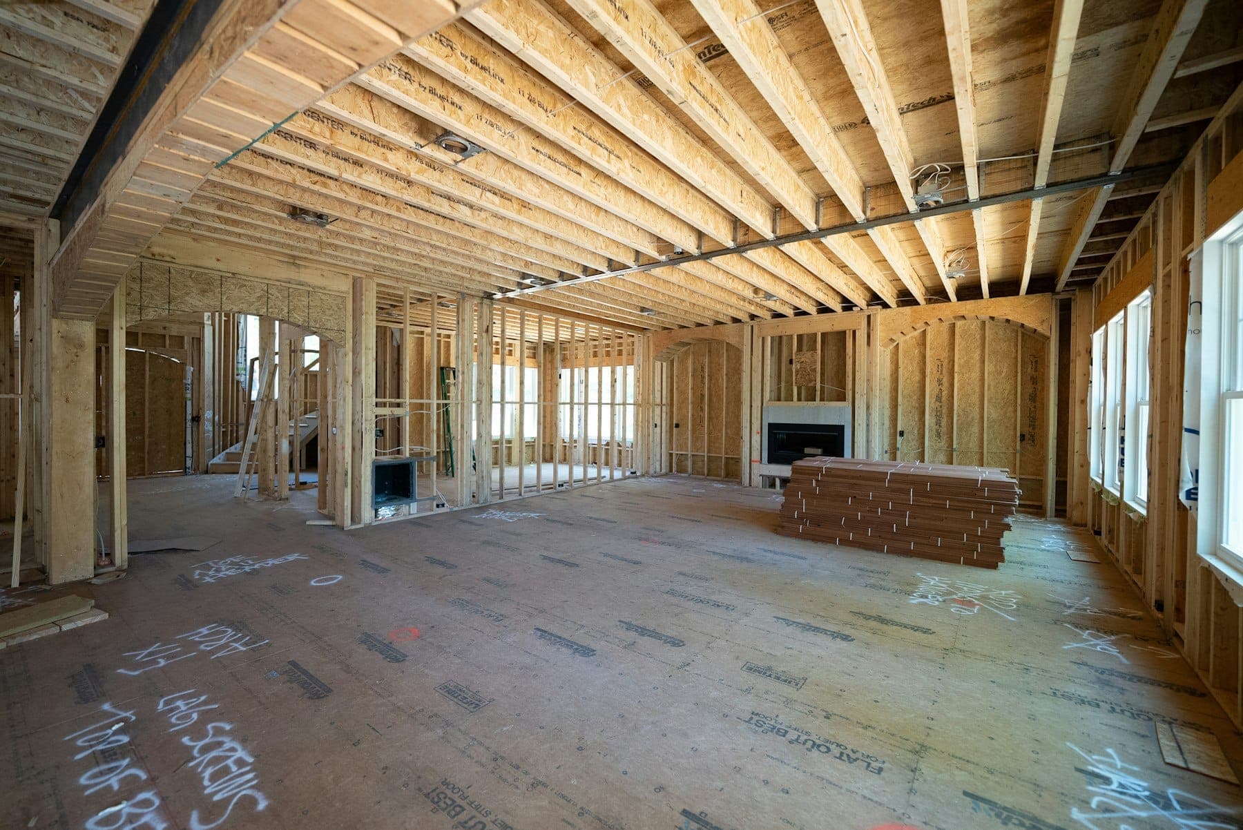 Open-plan interior mid-build with exposed floor joists, wood stud walls, stacked flooring and a fireplace rough-in
