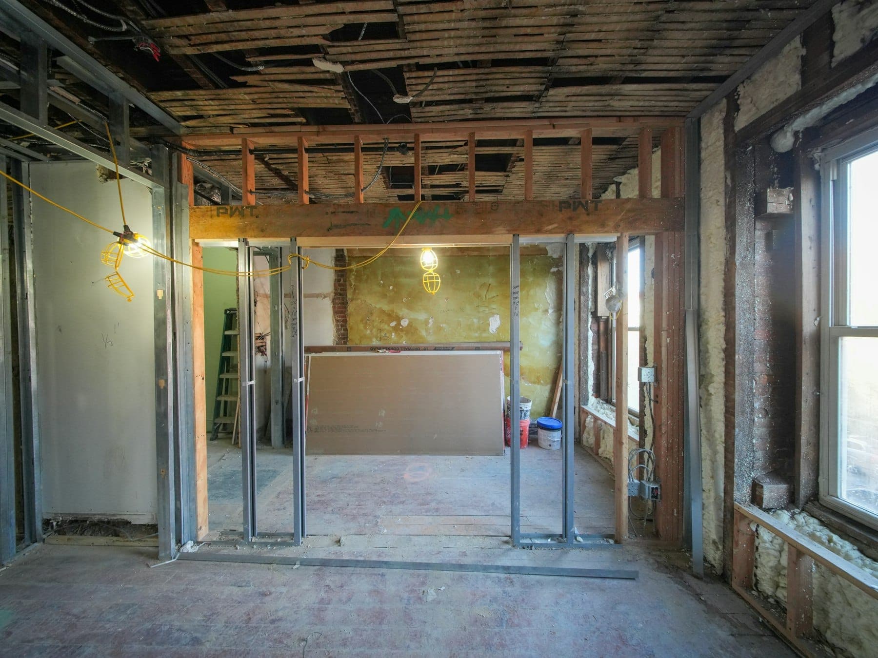 Gutted room mid-renovation with new partition framing, spray-foam insulated exterior walls and drywall sheets staged