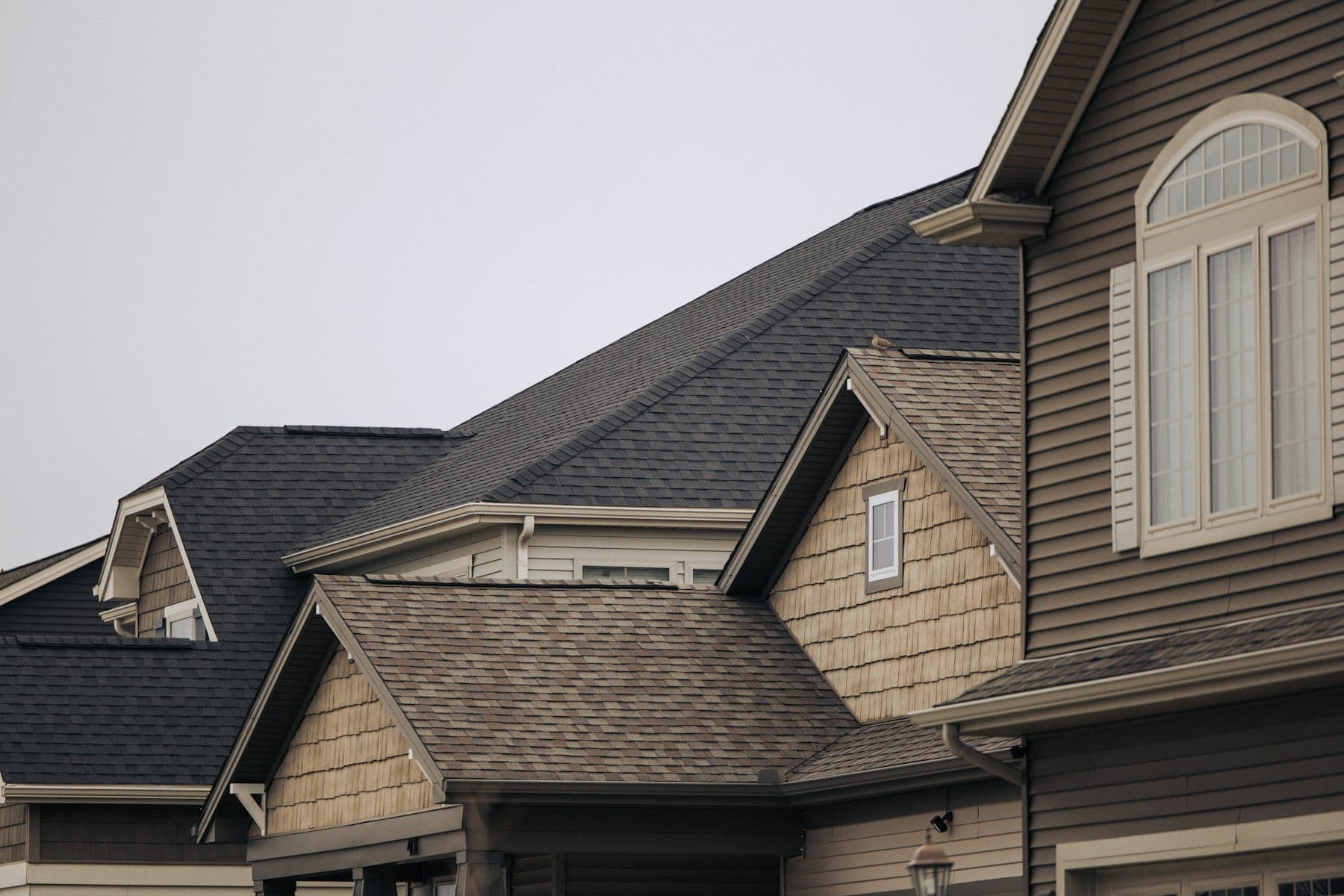Intersecting gables and valleys on a two-storey home with dark asphalt shingles, lap siding and shake accents