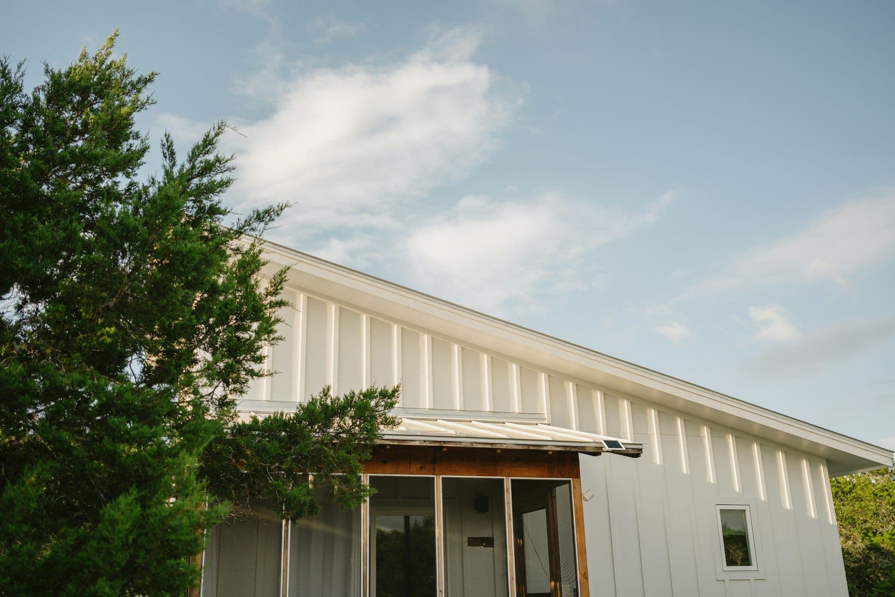 White board-and-batten exterior of a modern farmhouse with a long roofline and a cedar-trimmed entry